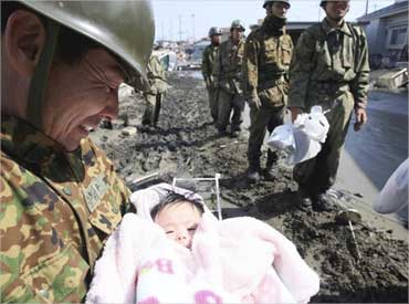 A Japan Self-Defense Forces officer holds a 4-month-old baby girl who was rescued along with her family members from their home in Ishimaki City.