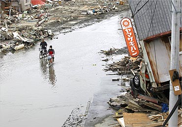 People ride their bicycles in a flooded road at an area destroyed by an earthquake.