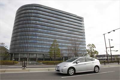 Toyota Motor Corp's Prius hybrid car travels in front of the company headquarters.