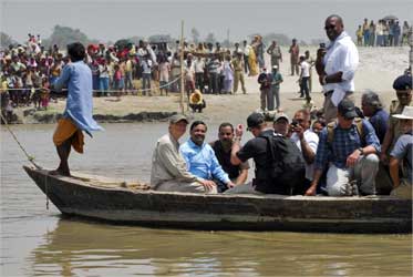 Gates (front 2nd L) sits in a boat as he crosses river Kosi in Bihar.