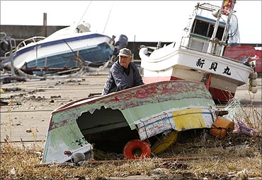 Fisherman Ryusuke Isogai in front of his ship (R) , which was washed onto the shore.
