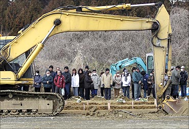 Family members of victims of the earthquake and tsunami watch as an excavator digs a mass grave.