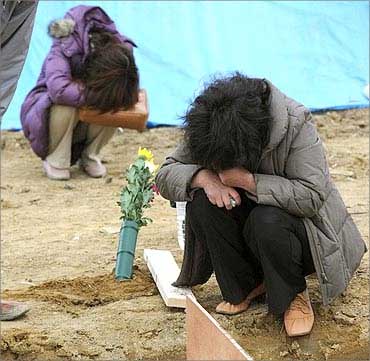 Survivors grieve at a grave of a victim of the March 11 earthquake at a mass grave.