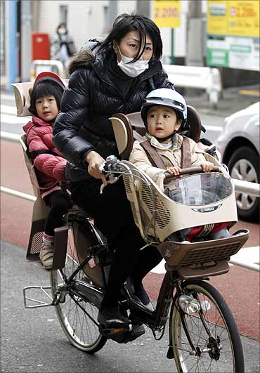 A woman and her children ride on a bicycle past a ward office in Tokyo.