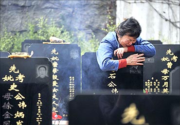 A woman cries as she hugs the tombstone of her husband at a public cemetery.
