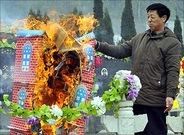 A man reacts as he burns a paper villa as an offering in front of tombstones of his ancestors.