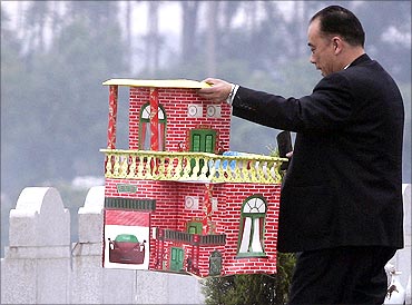 A man holds a paper house as he prepares to burn it as an offering to his ancestors at a cemetery.