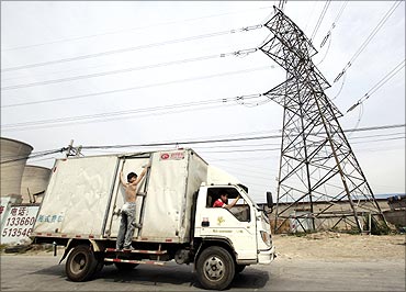 A truck carrying a man drives past electricity wires near a coal-fired power plant.