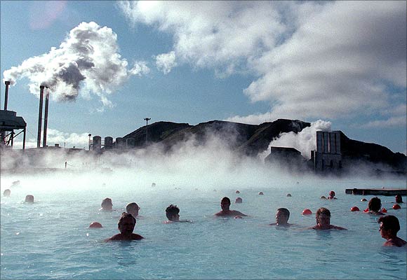 Bathers at the Blue Lagoon hot springs swim in hot mineral waters amid a chilly wind as a thermal electricity plant looms in the background.