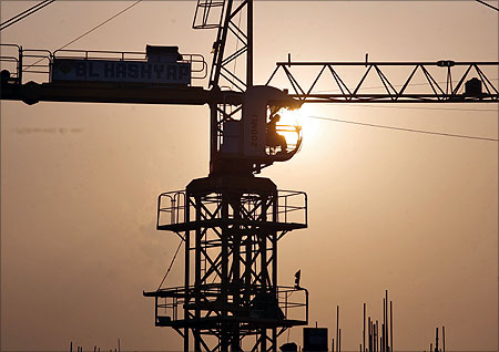 A worker sits inside a crane is silhouetted against the setting sun at the construction site of a commercial complex in Noida.