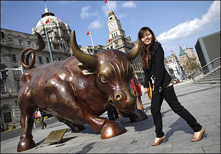 A woman poses next to a bull statue known as the Bund Financial Bull along the Huangpu River in Shanghai.