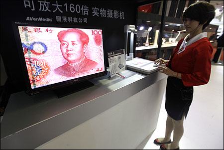 An employee operates a camera to zoom in on the image of a Chinese one-hundred yuan banknote.