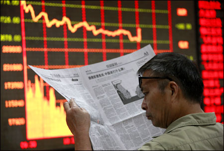 An investor reads a newspaper in front of an electrical board showing stock information at a brokerage house in Huaibei.