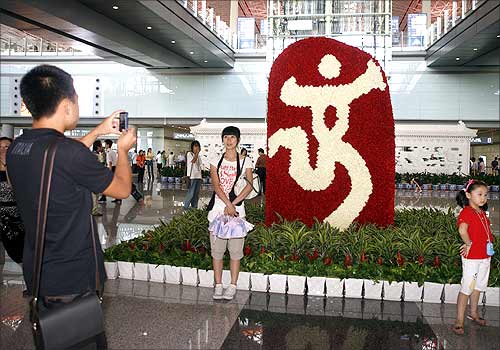 Travellers pose near a Beijing Olympic emblem at Beijing airport.