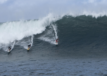 Three surfers catch a large wave in Haleiwa, Hawaii.