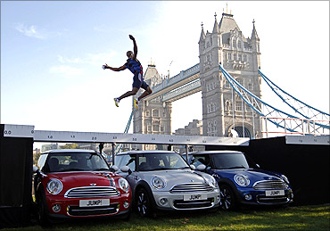 British long jumper J.J. Jegede jumps over three Mini cars, next to Tower Bridge.