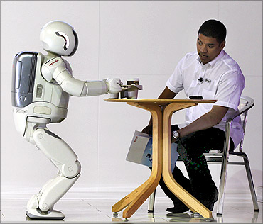 ASIMO, a humanoid robot created by Honda, serves tea to a visitor.