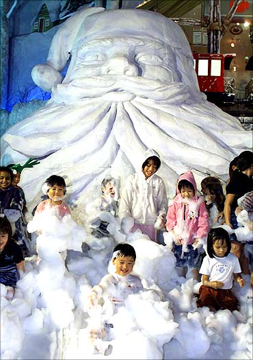 Singaporean children frolic in imitation snow under a giant Santa Claus outside a shopping mall.
