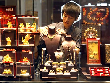 An employee adjusts a gold necklace on a displaying model near glass cases containing gold figurines at a gold shop in Wuhan.