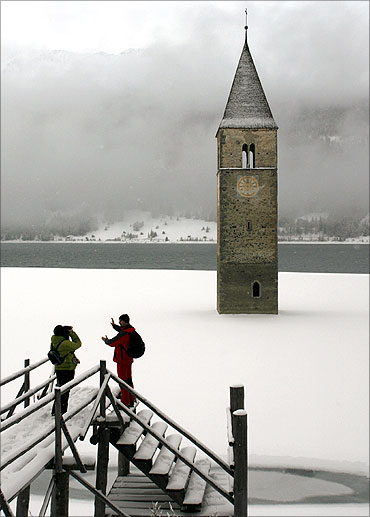 People take pictures in front of the former church tower of the Village of Graun in South Tyrol.