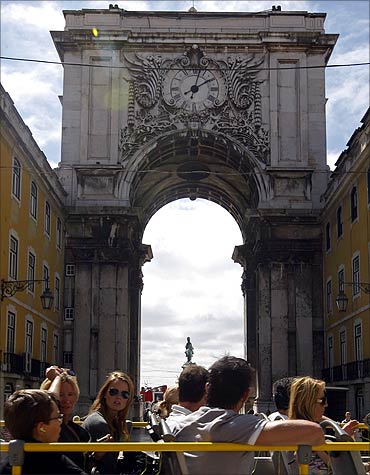 Tourists ride a tourist bus in front of Lisbon's main arcade of Praca do Comercio.