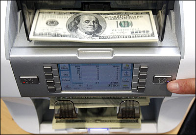 A bank clerk starts a money counter to count 100 dollar banknotes in a bank.