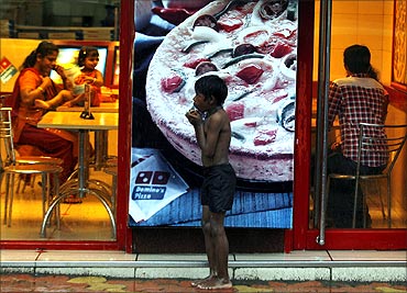 A homeless boy holds biscuits that he received as alms as he takes shelter from rain in front of a fast food shop in Mumbai.
