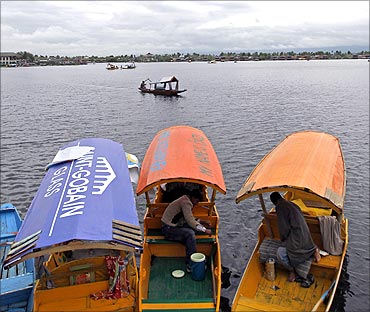 Kashmiri boatmen rest in their boats, against the backdrop of the cloudy sky in Srinagar.