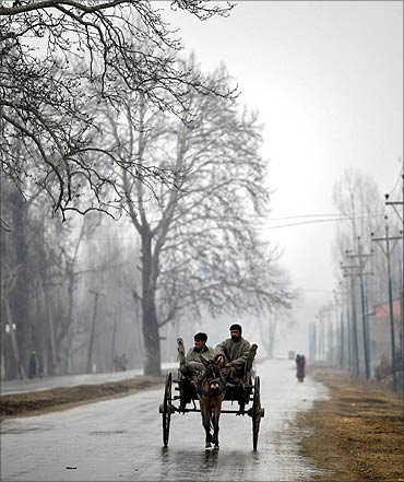Kashmiri people travel on a mule-driven cart on a cold day in the outskirts of Srinagar.