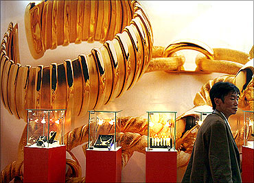 A visitor to the China International Jewellery Fair walks past a poster and gold jewellery display in Beijing.