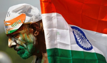 A supporter of activist Anna Hazare with a painted face stands next to an Indian national flag at the Ramlila grounds.