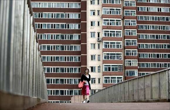 A women walks on a pedestrian bridge in front of a residential building in Beijing.