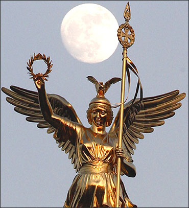 The moon is pictured beside the Golden Victoria on top of the victory column in Berlin.