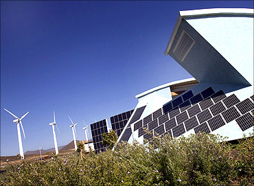 The solar panels of a bioclimatic house are seen next to windmills.