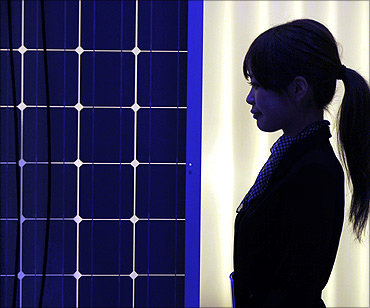 A woman is silhouetted next to a solar panel display by solar module supplier in Tokyo.