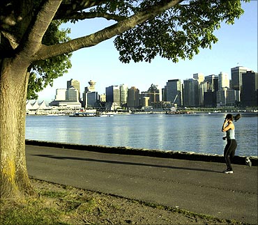 A jogger runs along the seawall in Stanley Park with the city skyline in the background.