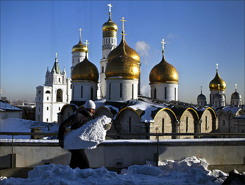 A worker cleans snow from a roof in front of the domes of the several several churches and cathedrals inside Moscow's Kremlin.