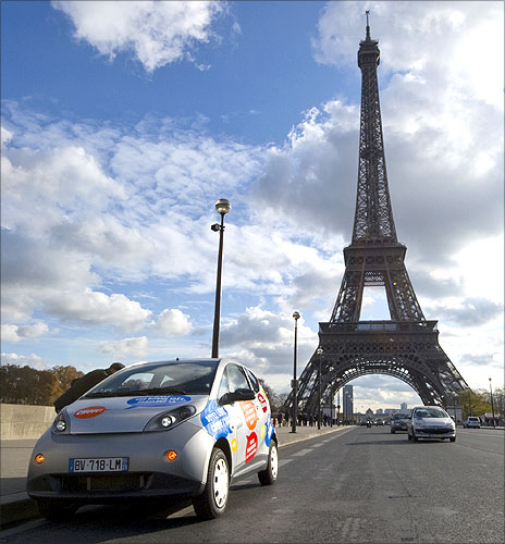 A Paris Autolib' electric car is parked next to the Eiffel tower.