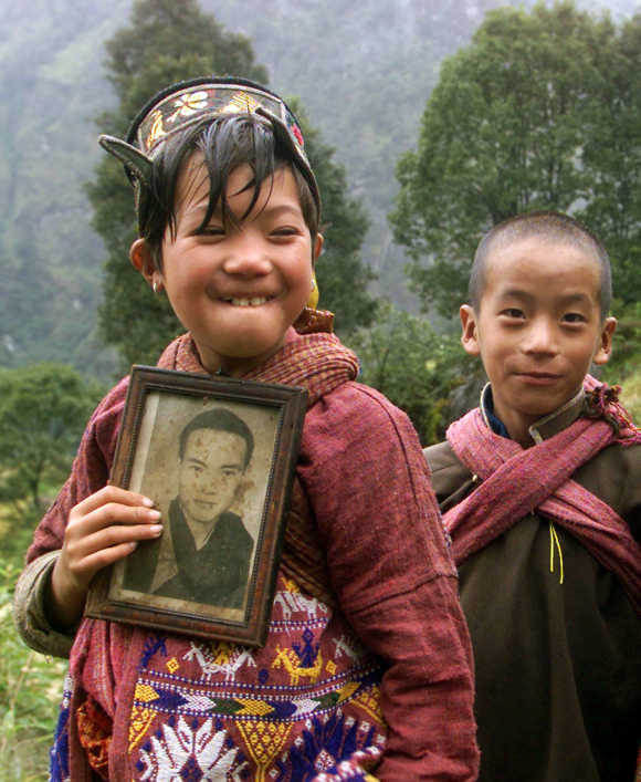 A Monpa tribal girl wearing traditional dress poses with a photograph of a Buddhist priest as her brother looks on in Tawang in Arunachal Pradesh.