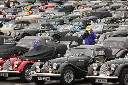 An enthusiast takes photographs amongst a large collection of Morgan sports cars.