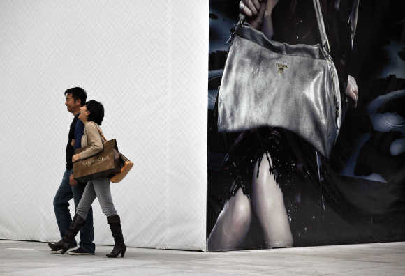 A couple walks past a poster advertising a luxury fashion brand after shopping on a main street in Shanghai.