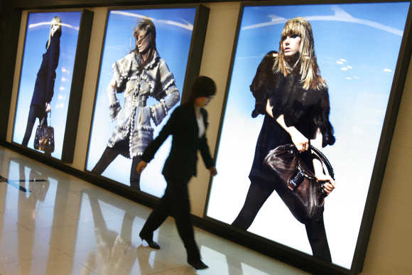 Woman walks past advertisements for designer clothes inside a shopping mall in Beijing.