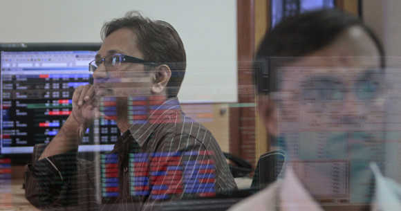 A broker watches a TV news channel as another monitors share prices at a brokerage firm in Mumbai.