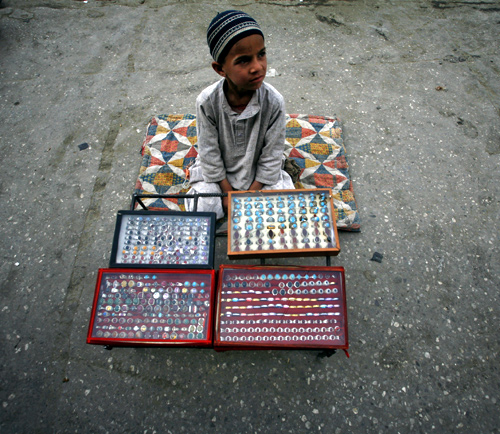 A boy waits for customers while sitting at his father's stall which sells metal rings at a roadside in Quetta.