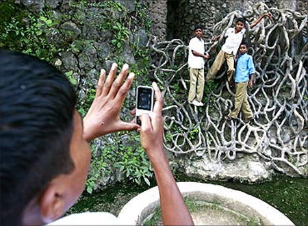 A schoolboy uses his cell phone to take a picture of classmates hanging onto cement roots at Nek Chand's Rock Garden in Chandigarh.