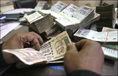 An employee counts rupee notes at a cash counter.