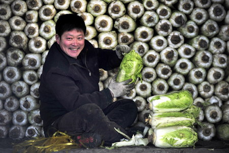 vendor smiles as he waits for customers in front of piles of Chinese cabbage at a vegetable wholesale market in Shenyang, Liaoning province.