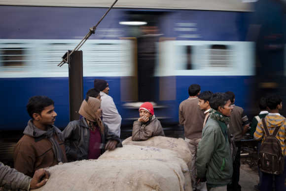 Workers wait to cross tracks as a train to passes nearby to the Nizamuddin Railway Station.
