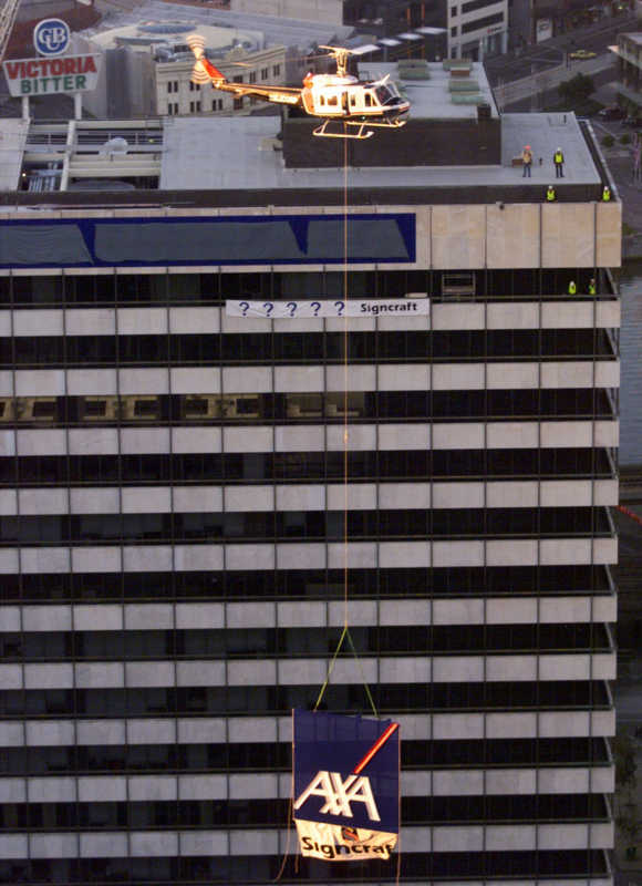 A helicopter lifts a six metres square AXA sign, one of two, weighing 1,500kg attached by a 150-foot-long steel cable to the roof of a building in Melbourne.