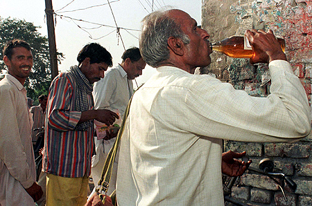A man gulps down liquor outside a wine shop while others stand in a queue to buy liquor in Rewari, Haryana.